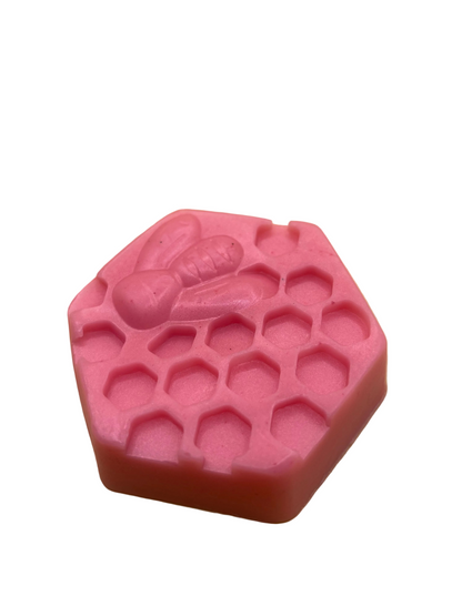 A pink hexagonal soap bar with a honeycomb pattern and a bee design on top.